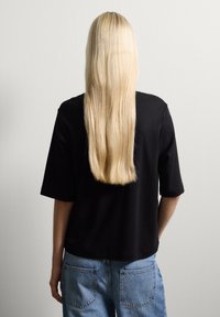 Top negro de manga corta con un corte holgado, combinado con jeans de mezclilla azul claro; textura suave y diseño sencillo. Se ven el cabello largo y liso.