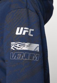 Felpa blu navy con motivo astratto nero. Presenta i loghi bianchi "UFC" e "VENUM" sulla spalla. Il materiale sembra morbido e con texture.