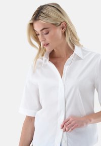 White short-sleeve button-up shirt with a classic collar, smooth texture, and a single row of buttons, showcasing a clean, minimal design.