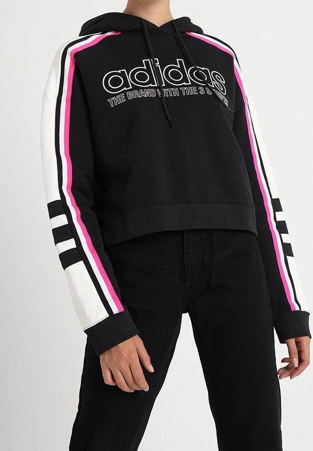 Černá zkrácená mikina s kapucí, s bílými a růžovými pruhy. Obsahuje velké logo "Adidas" a design tří pruhů na rukávech. Měkká textilie.