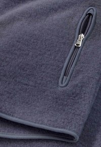 Coperta di pile grigia con una superficie testurizzata, caratterizzata da una cerniera scura a contrasto su un lato e bordi cuciti per la durabilità.