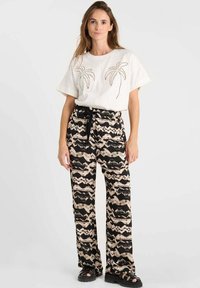 T-shirt blanc avec broderie de palmier et pantalon large à motifs noir et beige ; tissu texturé avec une ceinture nouée. Sandales noires.