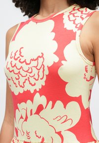 Detailný záber na šaty bez rukávov s rebrovanou textúrou, zdobené veľkými krémovými a koralovými kvetinovými vzormi na koralovom pozadí.