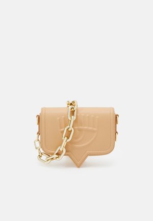 Beżowa skórzana torba na ramię z tłoczonym wzorem oka i masywnym złotym łańcuszkiem, prostokątna z zaostrzonym dolnym brzegiem.