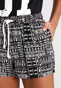 Shorts à motifs noirs et blancs avec une ceinture élastique, un cordon de serrage et des poches latérales présentant des dessins géométriques et des motifs tribaux.