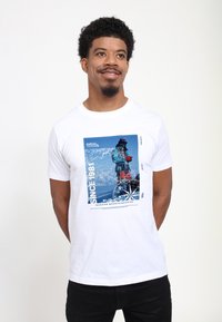 Biała bawełniana koszulka z graficznym nadrukiem w odcieniach niebieskiego, przedstawiającym krajobraz górski, z napisem "SINCE 1981" oraz "DURHAM MOUNTAINEERING" w kolorze czarnym.