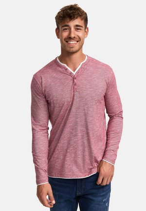 Rød tekstureret skjorte med lange ærmer, hvid krave og tre-knaps placket, parret med blå jeans.