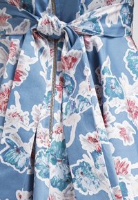 Robe à motifs floraux en tissu bleu clair avec des designs blancs, roses et verts. Elle dispose d'une ceinture à nouer et d'un zip visible.