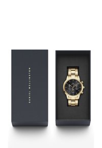 Orologio in metallo dorato con quadrante nero caratterizzato da dettagli argentati, esposto in una scatola blu navy con il nome del marchio "Daniel Wellington" impresso.