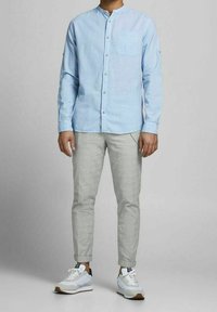 Světle modrá košile s dlouhým rukávem, s límečkem na knoflíky a náprsní kapsou, v kombinaci se světle šedými zúženými kalhotami a bílými teniskami s akcenty.