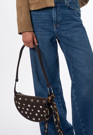 Sac à main en cuir marron avec découpes circulaires, en forme de demi-lune, anses courtes, et une écharpe à imprimé léopard attachée à la sangle.