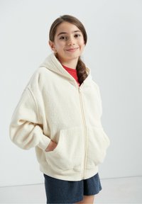 Sweat à capuche en polaire couleur crème avec une fermeture éclair frontale, de grandes poches et une coupe ample. Doté d'une capuche et d'un tissu doux et texturé.