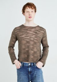 Brun, texturerad, långärmad stickad tröja med en avslappnad passform, ihop med blå denimjeans. Tröjan har ett subtilt horisontellt mönster.