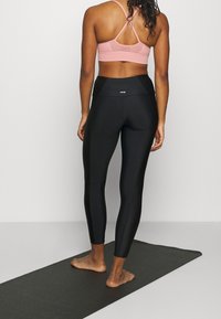 Svarta leggings med hög midja och rosa sport-bh med meshinlägg baktill, som visar en slank design och figurnära textur, lämpliga för idrottsbruk.