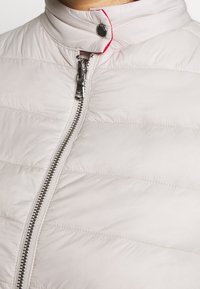 Světle šedá péřová bunda s horizontálním prošíváním, předním zapínáním na zip, stojáčkem a kontrastním červeným detailem na límci.
