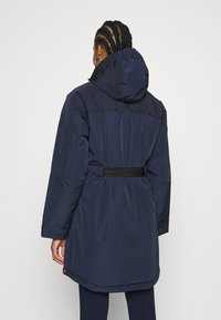 Granatowa puchowa kurtka z kapturem, z paskiem w talii i gładką teksturą. Charakteryzuje się kontrastującą górną częścią oraz elastycznym paskiem z tyłu.