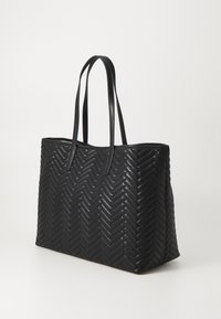 Sac fourre-tout en cuir noir avec un motif chevron, de forme rectangulaire et deux longues poignées. Surface texturée avec des accents lisses.