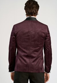 Burgundy mönstrad kavaj med subtil paisleymönster, enknappsstängning, svarta slag och kontrasterande ärmar. Slät textur med skräddarsydd passform.