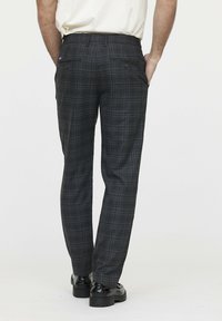 Pantalons à carreaux gris avec une coupe décontractée, présentant une texture lisse, deux poches arrière et des accents foncés, associés à des chaussures noires.