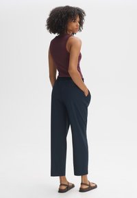 Bordeaux mouwloos topje gecombineerd met marineblauwe elastische broek. Het model heeft krullend haar en staat op met bruine sandaaltjes met straps.