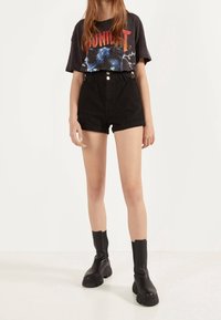 Svart grafisk t-shirt med ett pantermotiv och text, kombinerad med högmidjade svarta shorts och kraftiga svarta ankelskor.