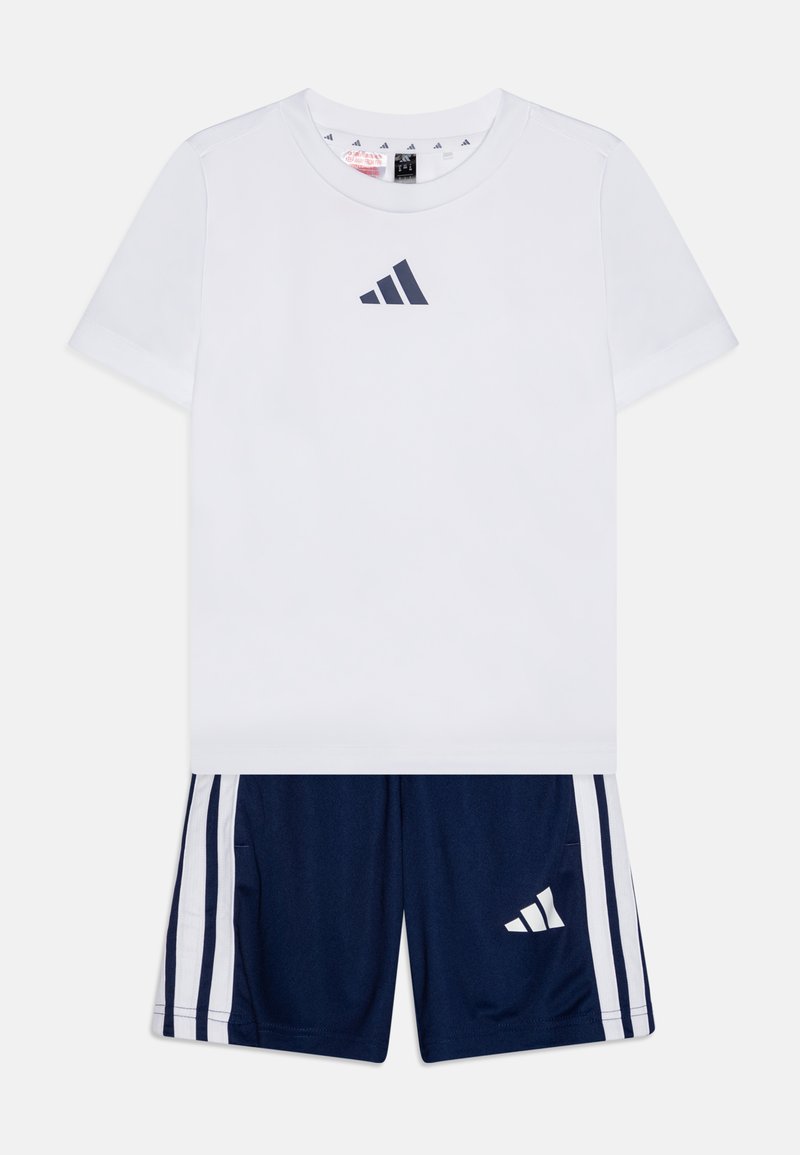 Camiseta blanca de manga corta con logo azul marino, combinada con pantalones cortos azul marino que tienen franjas laterales blancas y un pequeño logo blanco en la pierna.