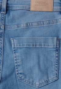 Vaqueros de denim azul claro que cuentan con un único bolsillo trasero con un borde superior curvado y una etiqueta de cuero etiquetada "Street One Denimatelier."