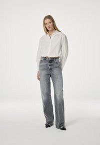 Witte cropped shirt met hartborduursel en knoopsluiting, gecombineerd met lichtgrijze, hooggetailleerde denim jeans met een vervaagde textuur.