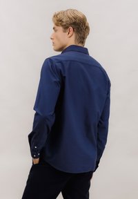 Marineblå skjorte med knapper, langermet, mykt bomullsstoff, rett passform, enkel knapp ved mansjettene, detalj på bakstykkeskjøtet.