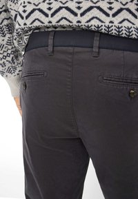 Pantaloni grigio scuro con una texture liscia, dotati di due tasche posteriori con chiusura a bottone e una vita a contrasto.