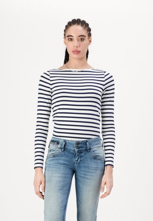 Chemise rayée à manches longues en marine et blanc, avec un col bateau. Assortie avec un jean bleu clair à finition légèrement déchirée.