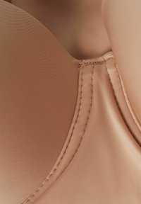 Nude beha van gladde, zachte stof. Heeft gevormde cups, dunne bandjes en verstevigde stiksels langs de randen voor ondersteuning en duurzaamheid.