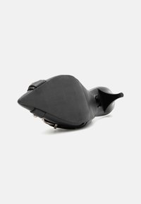 Sapato de salto alto preto com bico apontado e textura mate suave. A sola é plana com uma curva subtil, apresentando detalhes de hardware mínimos.