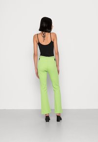 Top preto de alças, combinado com calças verdes brilhantes de boca de sino, apresentando uma cintura ajustada e um tecido texturizado. Sapatos pretos de salto completam o visual.