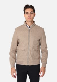 Giacca in misto lana beige con orlo a coste, chiusura con zip e due tasche frontali a patta con dettagli a bottoni. Collo alla coreana, silhouette aderente.
