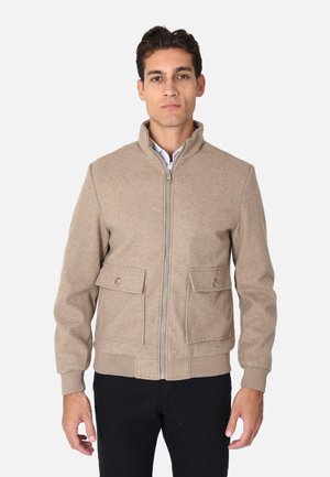 Giacca in misto lana beige con orlo a coste, chiusura con zip e due tasche frontali a patta con dettagli a bottoni. Collo alla coreana, silhouette aderente.