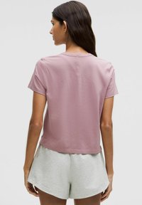 Camiseta rosa de manga corta con cuello redondo y un corte relajado, combinada con pantalones cortos gris claro. Material de algodón suave.