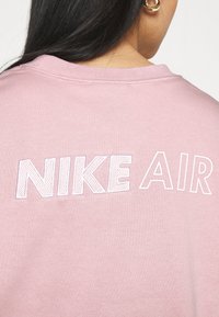 Felpa rosa con il logo "NIKE AIR" ricamato in bianco sulla schiena. Presenta un collo rotondo e un tessuto morbido e texturizzato.