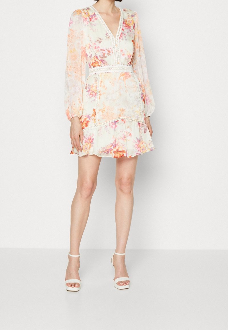 Robe à imprimé floral avec un décolleté en V, des manches longues bouffantes et un ourlet à volants superposé. Fond crème avec des accents orange et rose.