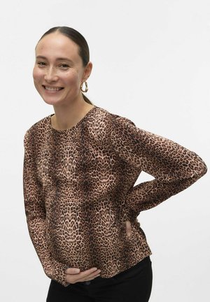 Leopardų rašto palaidinė iš tampraus audinio, su ilgomis rankovėmis ir apvalia iškirpte, derinama su juodomis kelnėmis. Modelis laiko savo pilvą.