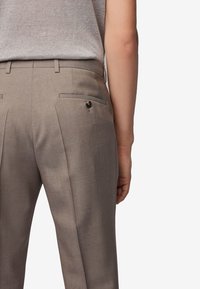 Jasnobrązowe spodnie wykonane z teksturowanej tkaniny, z płaskim frontem, dwoma tylnymi kieszeniami, z których jedna ozdobiona jest guzikiem, o dopasowanym kroju.