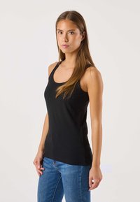 Svart linne med rundad halsringning och tunna band, tillverkat av mjukt material. Kombinerat med blå tajta jeans.