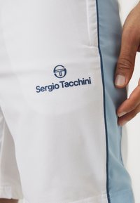 Witte sportshorts van een gestructureerde stof, met blauwe accenten aan de zijkant en een blauw logo met de tekst "Sergio Tacchini" aan de voorkant.