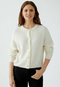 Helle beige Strickjacke aus weichem Material. Verfügt über einen runden Ausschnitt, gerippte Bündchen und eine Knopfleiste auf der Vorderseite.