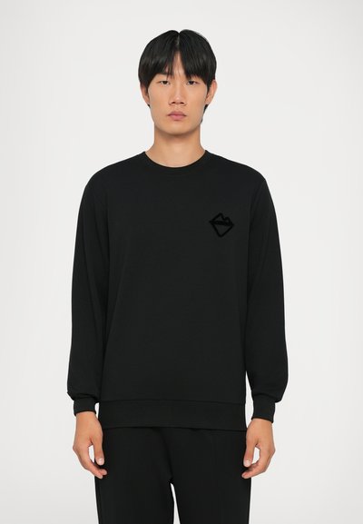 Sort sweatshirt lavet af blødt materiale, med rund halsudskæring, lange ærmer og et tekstureret sort logo på venstre bryst.