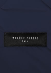 Donkerblauwe stof met een gestructureerd zwart etiket waarop witte tekst staat die luidt: "WERNER CHRIST BABY." Eenvoudig ontwerp, strakke lijnen.
