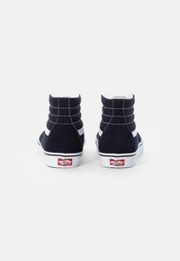 Černé semišové vysoké sneakers s bílými akcenty, viditelným švem, polstrovaným límcem a ikonickým červenobílým logem na patě.