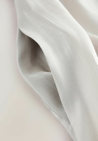 Ljusgrått tyg med en slät, sidenliknande textur som faller elegant. Materialet ser fint ut och är något reflekterande, med subtila veck.