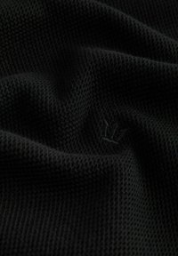 Tissu noir texturé avec un motif tissé subtil et un petit logo de couronne brodé sur la surface.