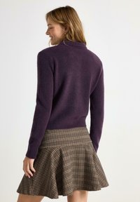 Lila, långärmad tröja gjord av mjukt material med ribbad nederkant. Matchad med en flare-skjorta i rutigt mönster med bruna och beige toner.